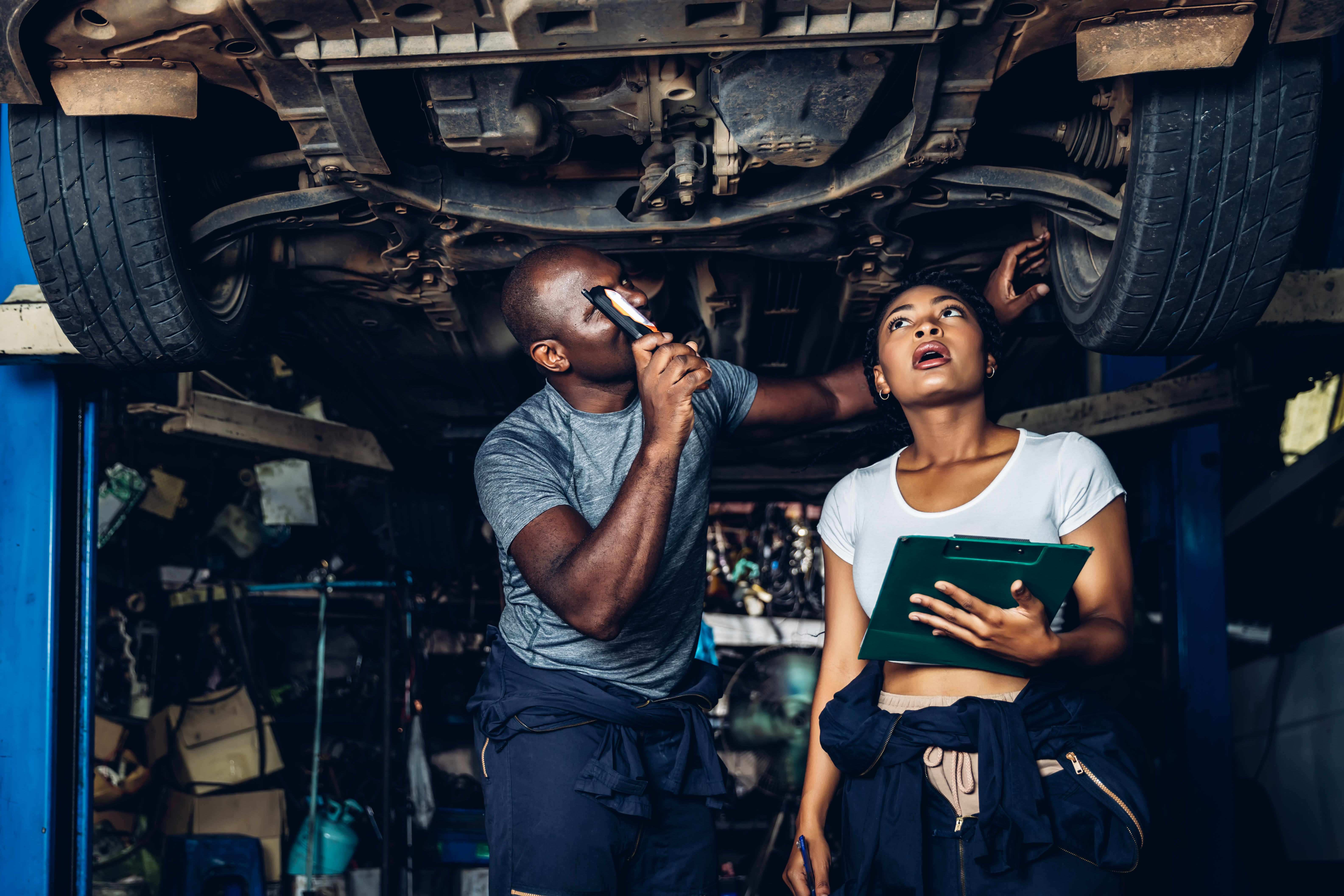 Two mechanics examine the underside of a car.